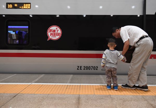 资料图片：9月21日，在北京南站，一名乘客在G1次“复兴号”列车前为孩子讲解火车知识。新华社记者李贺摄