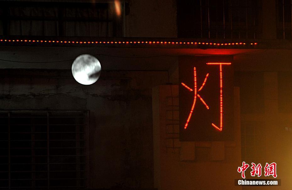 12月13日晚，福州上空的“超级月亮”和街头的广告灯。（多重曝光）当晚，继今年10月17日和11月14日之后，“超级月亮”再次现身天宇。这是今年以来，月球第三次最接近地球。中新社记者 张斌 摄