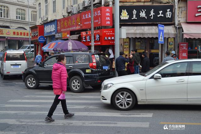 中山路上,一名行人正在过马路,白色轿车疾驶而过