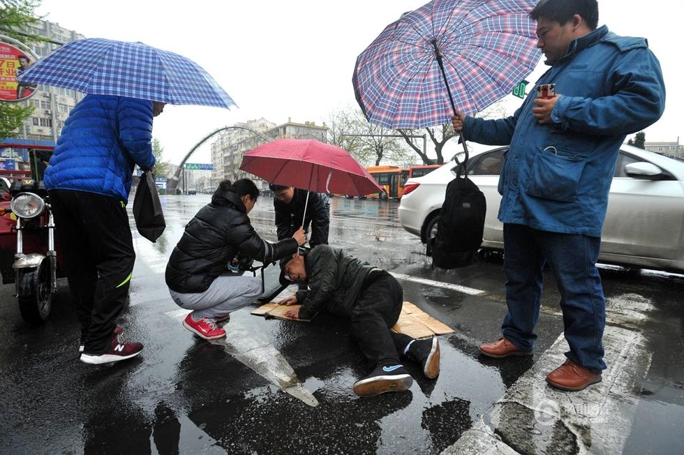 组图:青岛一老人路上摔倒 众人雨中为其撑伞