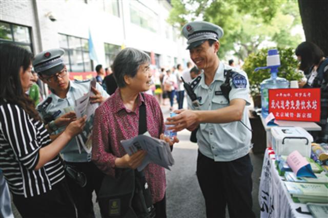 高考首日,城管队员为等候在考场外的考生家长送上新京报和矿泉水。新京报记者 浦峰 摄